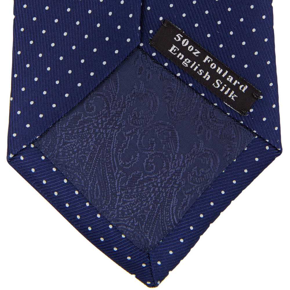 The Blue and White Small Spot Printed Silk Tie by Turnbull & Asser, shown rolled on a white background, features a refined white polka dot pattern—ideal for complementing any office shirt.