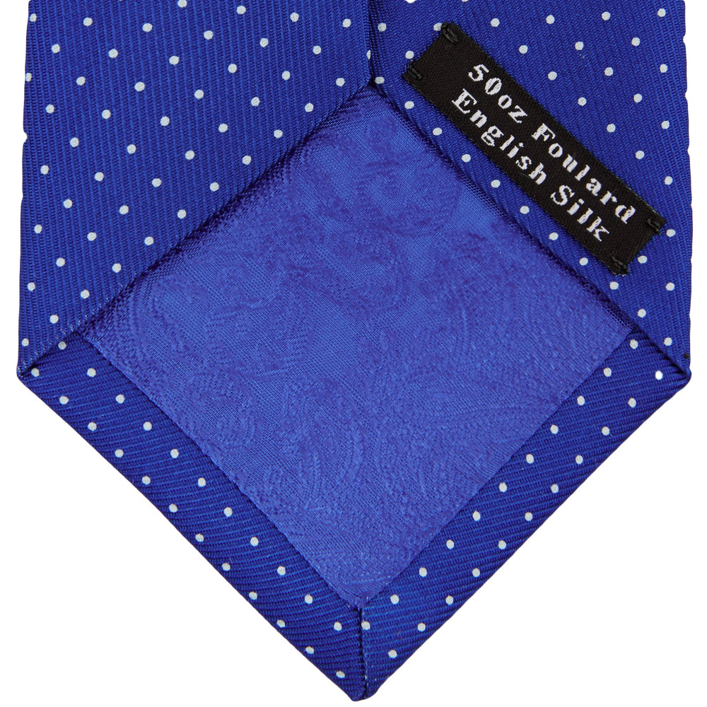 The Turnbull & Asser Slim Royal Blue and White Small Spot Printed Silk Tie, featuring white polka dots, is ideal for office wear and shown rolled up on a plain white background.