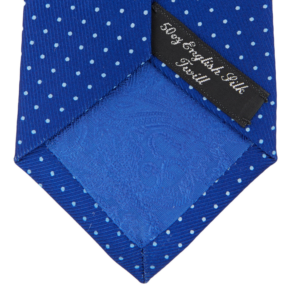 The Turnbull & Asser Royal Blue and White Small Spot Printed Silk Tie, shown rolled on a white background, features a refined spot pattern—ideal for complementing your office shirt.