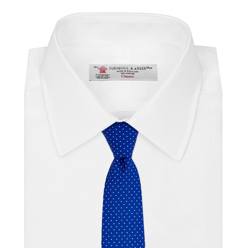 The Turnbull & Asser Slim Royal Blue and White Small Spot Printed Silk Tie, featuring white polka dots, is ideal for office wear and shown rolled up on a plain white background.