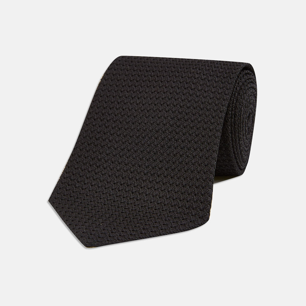 The Slim Black Grenadine Silk Tie by Turnbull & Asser, featuring a unique textured weave, is rolled up and displayed against a plain white background.