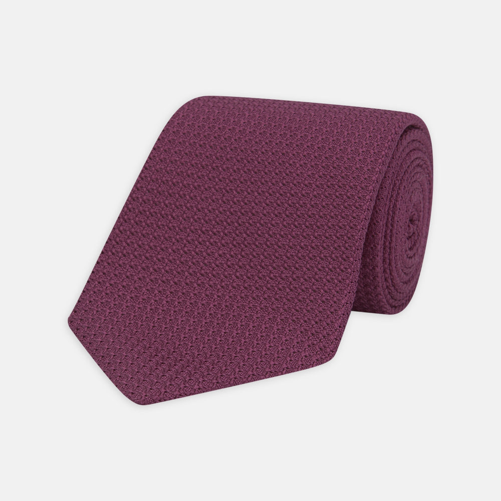 The Turnbull & Asser Wine Grenadine Silk Tie, featuring a textured weave in dark purple, is displayed rolled-up on a plain white background.