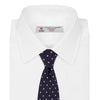 View 2 of product The Seven-Fold Navy Churchill Spot Silk Tie by Turnbull & Asser features evenly spaced white polka dots on navy silk—a luxury neckwear piece rolled up and displayed on a white background.