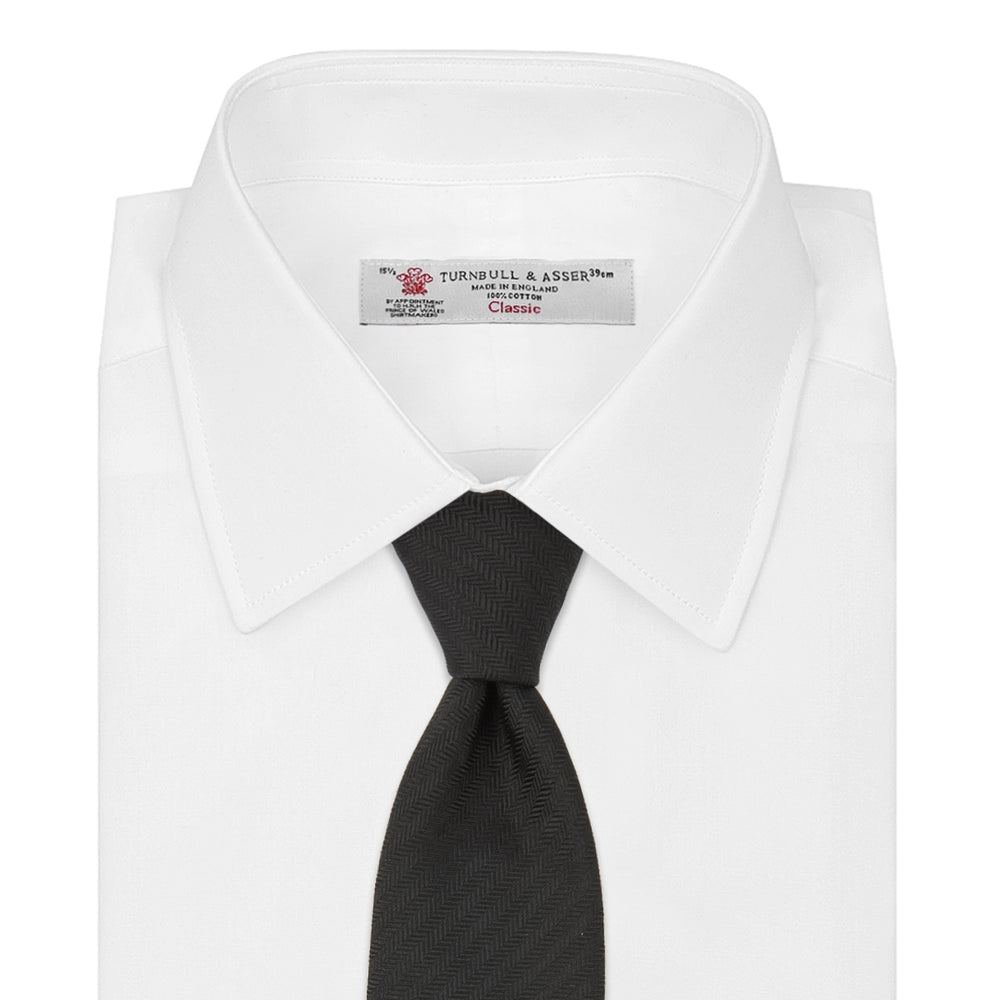 The Turnbull & Asser Slim Black Herringbone Silk Tie is neatly rolled, showcasing its subtle weave on a plain white background.