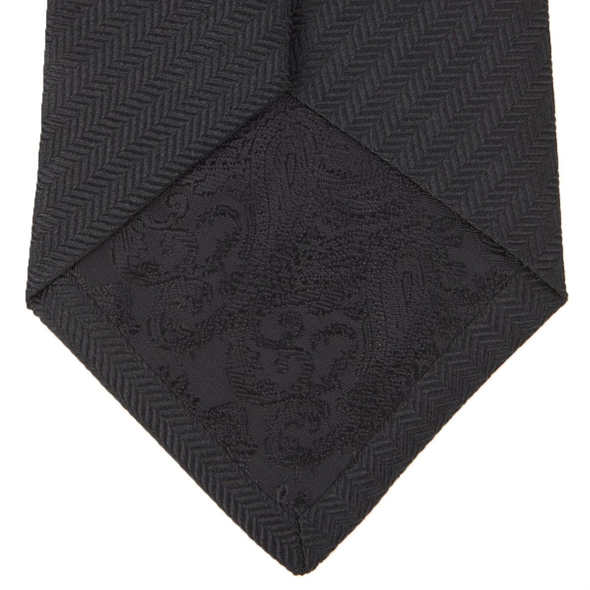 View 4 of product The Turnbull & Asser Slim Black Herringbone Silk Tie is neatly rolled, showcasing its subtle weave on a plain white background.
