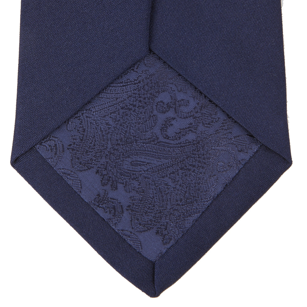 The Turnbull & Asser Seven-Fold Navy Plain Satin Silk Tie is neatly rolled and showcased against a plain light gray background.