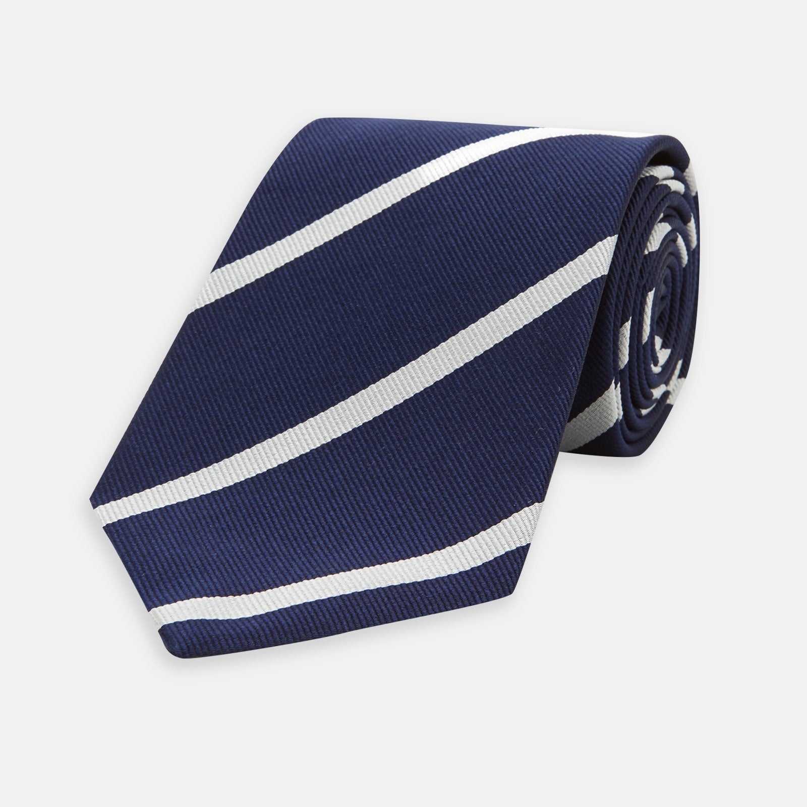 View 1 of product The Turnbull & Asser Long Navy and White Blazer Stripe Repp Silk Tie is shown rolled at one end, highlighting its diagonal stripes, against a plain white background.