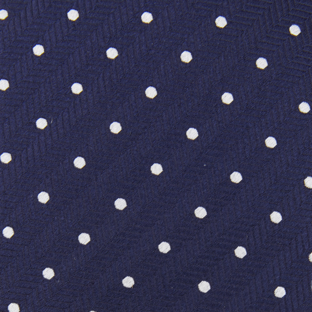 The Turnbull & Asser Seven-Fold Navy & White Spot Herringbone Silk Tie features a navy base with white polka dots and a classic herringbone weave, displayed rolled up on a plain white background.