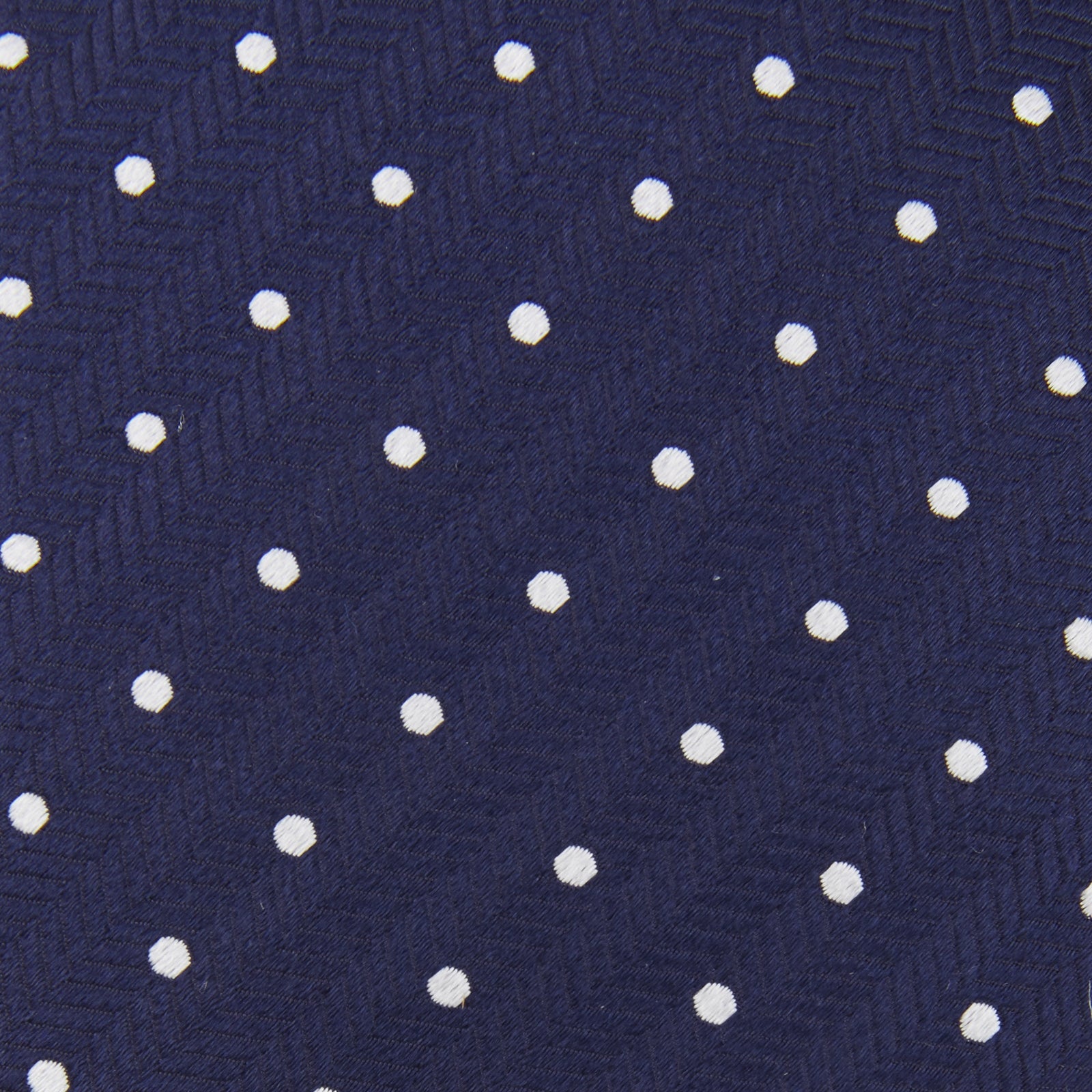 View 4 of product The Turnbull & Asser Seven-Fold Navy & White Spot Herringbone Silk Tie features a navy base with white polka dots and a classic herringbone weave, displayed rolled up on a plain white background.