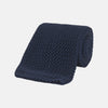 View 1 of product The Turnbull & Asser Navy Knitted Silk Tie features a textured open weave and flat squared ends, making it a versatile accessory for the modern gentleman’s wardrobe. Shown rolled up on a plain white background.