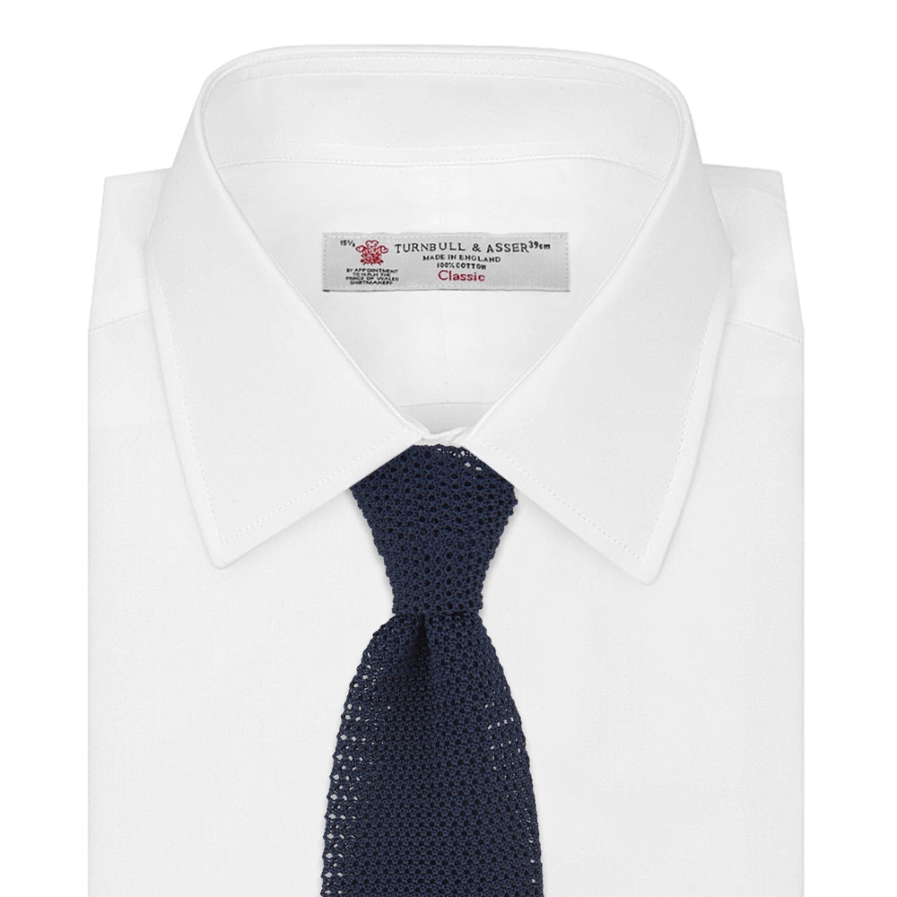 The Turnbull & Asser Navy Knitted Silk Tie features a textured open weave and flat squared ends, making it a versatile accessory for the modern gentleman’s wardrobe. Shown rolled up on a plain white background.