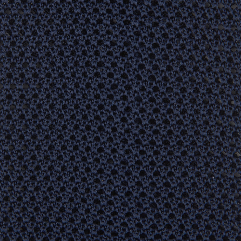 The Turnbull & Asser Navy Knitted Silk Tie features a textured open weave and flat squared ends, making it a versatile accessory for the modern gentleman’s wardrobe. Shown rolled up on a plain white background.