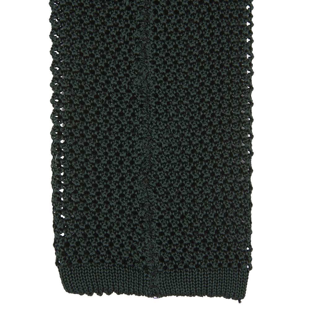 The Turnbull & Asser Green Knitted Silk Tie features a rich dark green hue and textured weave, making it an elegant accessory for any gentleman's wardrobe, shown rolled up against a light background.