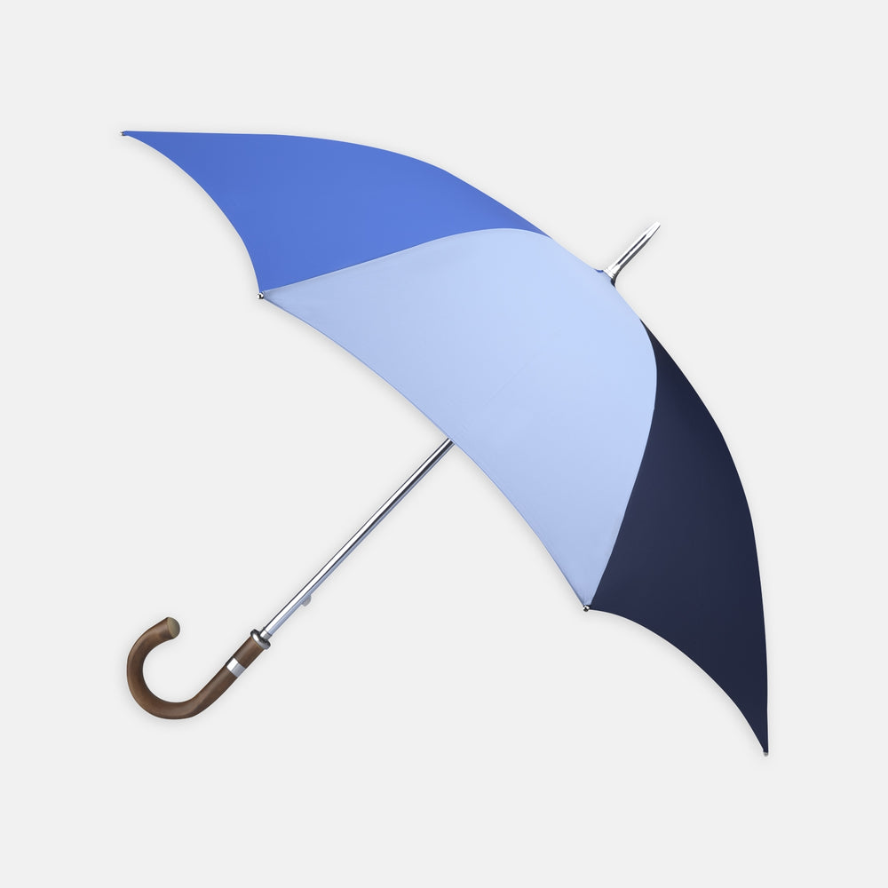 The Turnbull & Asser Sky, Royal Blue and Navy Umbrella with Chestnut Crook features alternating blue panels, a chestnut curved handle, and a silver shaft, making it stand out against a plain white background.