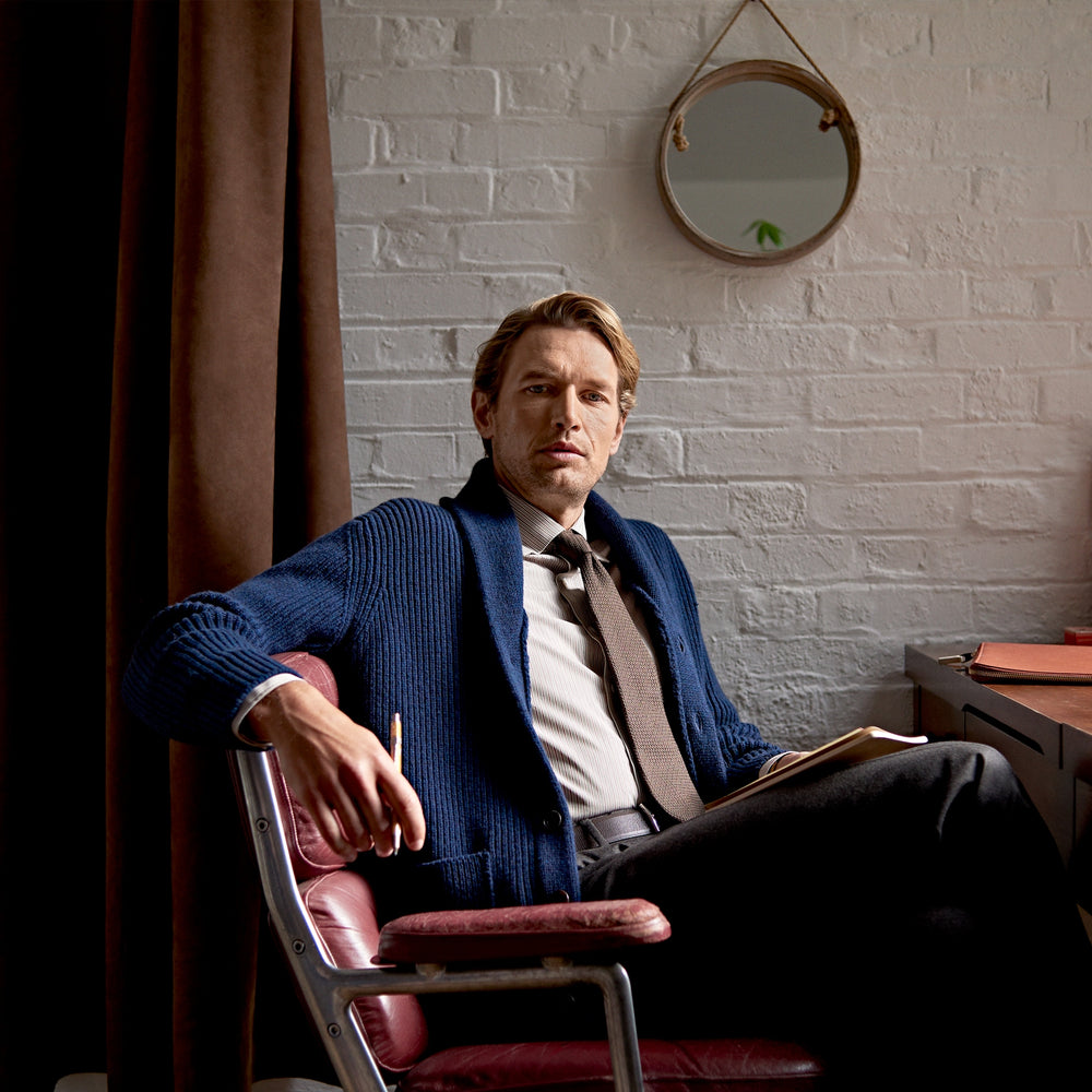 The Turnbull & Asser Navy Shawl Collar Cashmere Cardigan features a chunky knit, ribbed texture, button front, and two pockets—a luxurious piece laid flat on a white background for warmth and style.