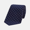 View 1 of product The Seven-Fold Navy and White Spot Lace Silk Tie by Turnbull & Asser showcases a luxurious navy silk with white spots, elegantly rolled and presented on a white background.