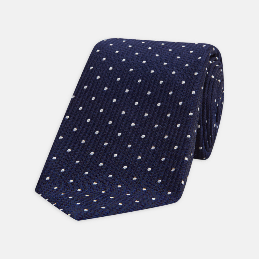 The Seven-Fold Navy and White Spot Lace Silk Tie by Turnbull & Asser showcases a luxurious navy silk with white spots, elegantly rolled and presented on a white background.