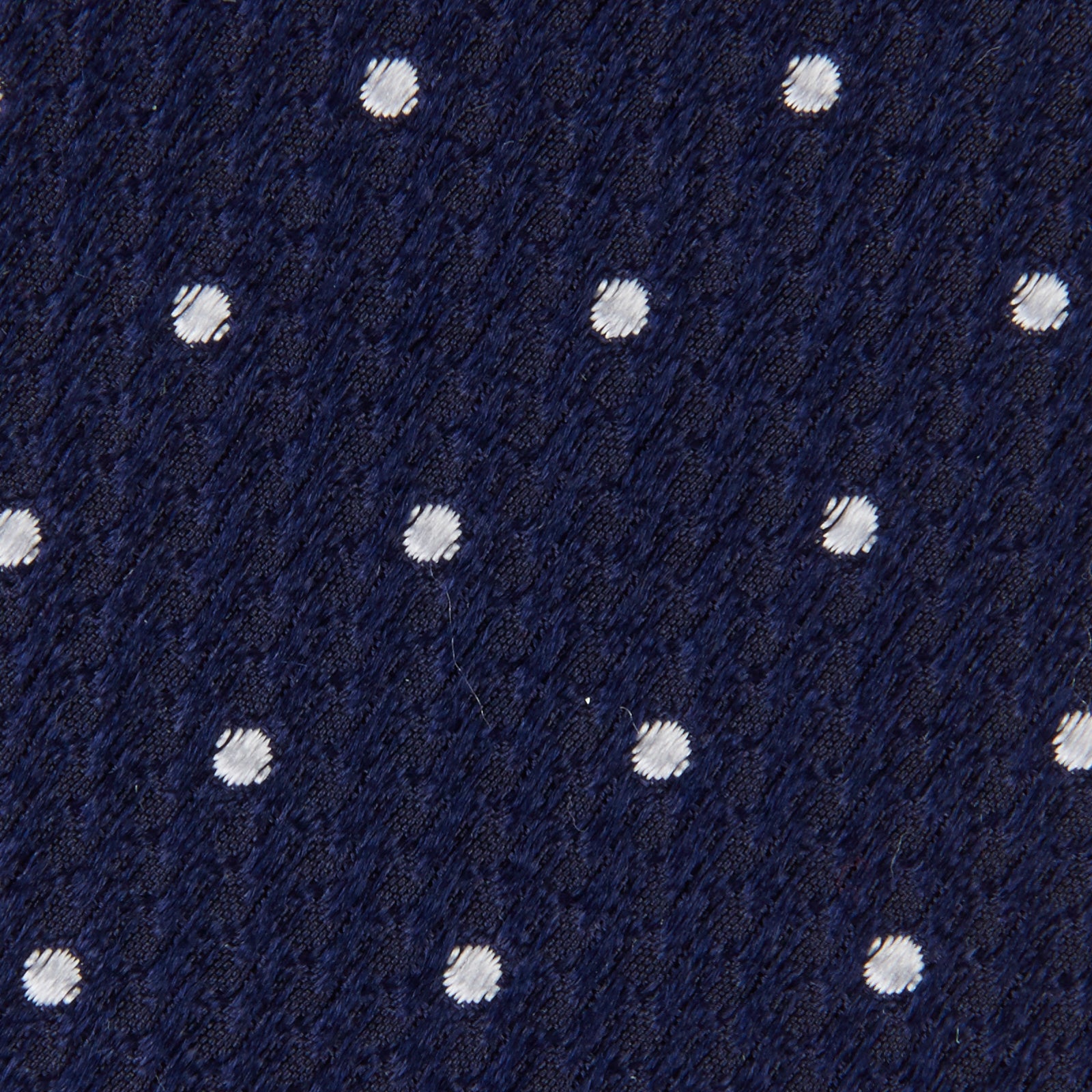 View 3 of product The Seven-Fold Navy and White Spot Lace Silk Tie by Turnbull & Asser showcases a luxurious navy silk with white spots, elegantly rolled and presented on a white background.