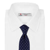 View 2 of product The Seven-Fold Navy and White Spot Lace Silk Tie by Turnbull & Asser showcases a luxurious navy silk with white spots, elegantly rolled and presented on a white background.
