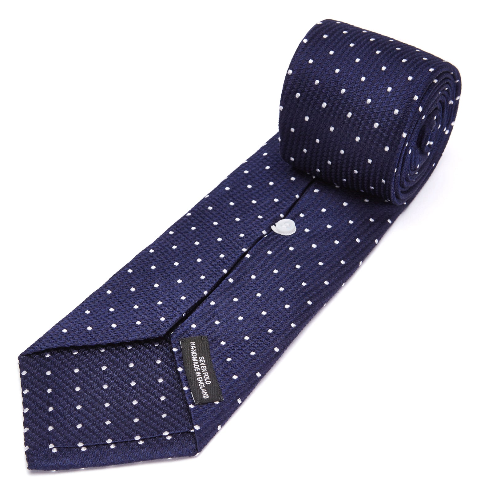 View 4 of product The Seven-Fold Navy and White Spot Lace Silk Tie by Turnbull & Asser showcases a luxurious navy silk with white spots, elegantly rolled and presented on a white background.