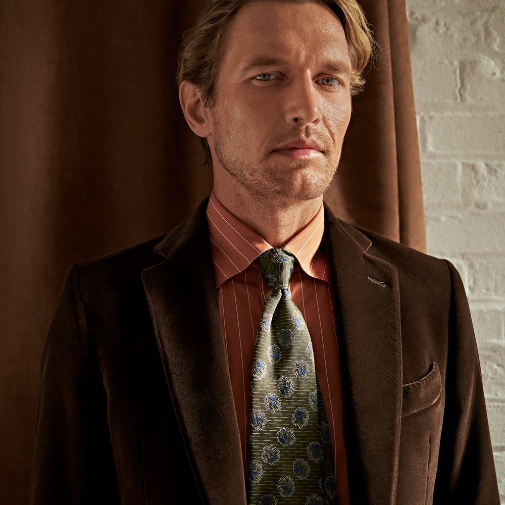 The Turnbull & Asser Brown Velvet Jacket for men features a notched lapel, two buttons, flap pockets, and a chest pocket, shown against a plain white background.