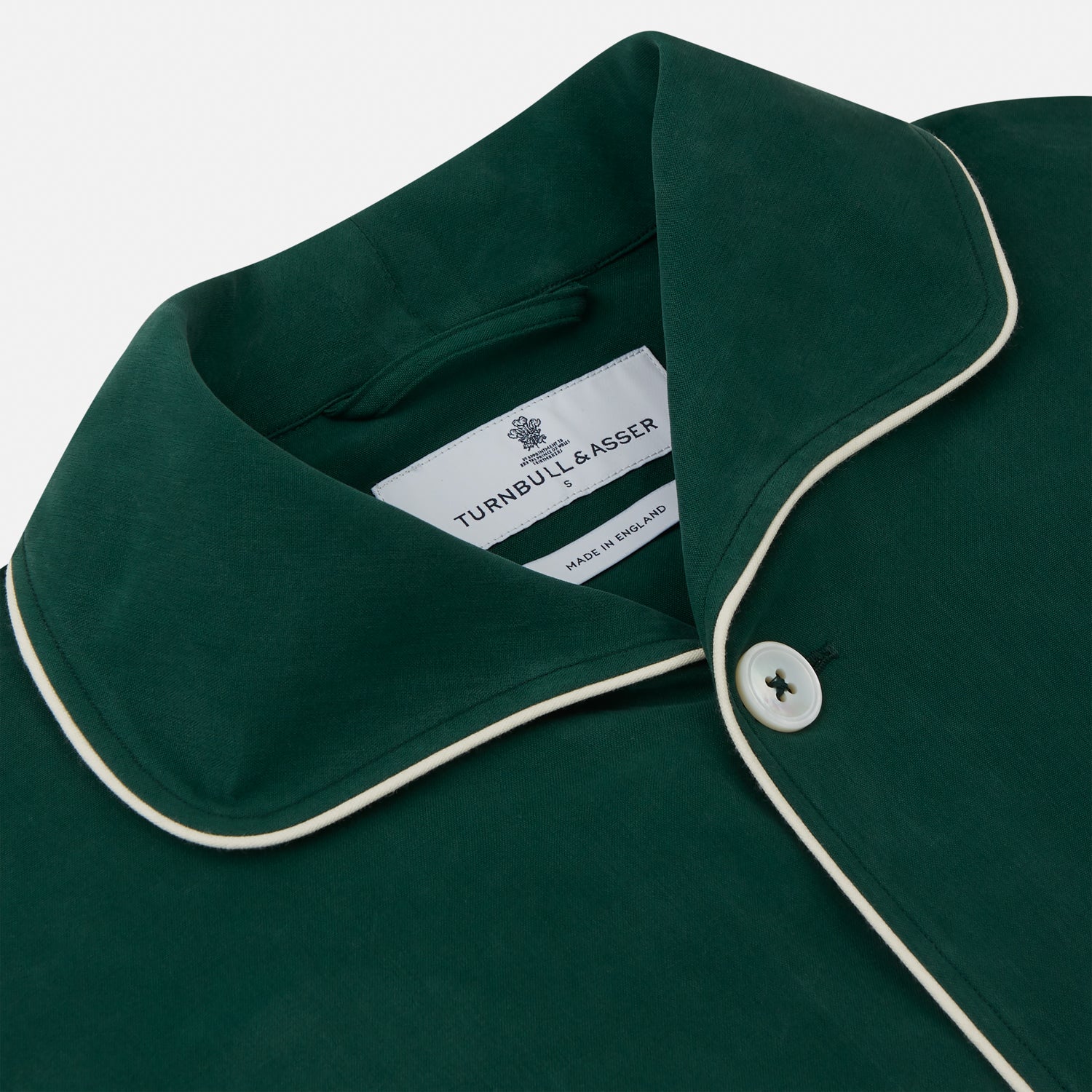 View 2 of product The Turnbull & Asser Dark Green Silk Pyjama Set features a long-sleeve button-up top with white piping, chest pocket, and matching pants, all neatly folded on a plain white background.
