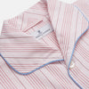 View 2 of product The Turnbull & Asser Pink And White Stripe Twill Cotton Pyjama Set features long sleeves and pants with a curved collar and blue trim on the cuffs, pocket, and hem—a classic gent’s style shown on a plain white background.