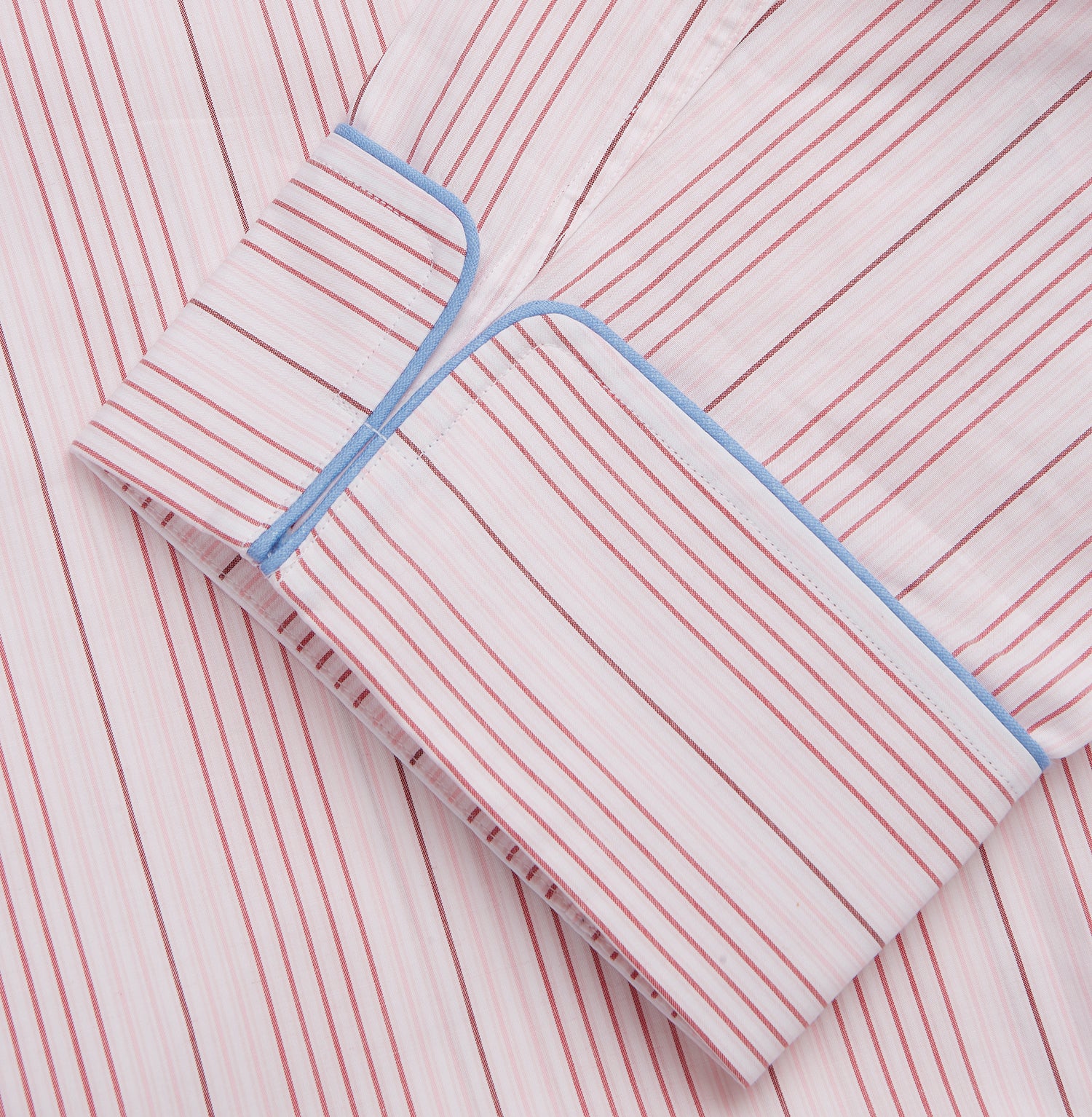 View 3 of product The Turnbull & Asser Pink And White Stripe Twill Cotton Pyjama Set features long sleeves and pants with a curved collar and blue trim on the cuffs, pocket, and hem—a classic gent’s style shown on a plain white background.