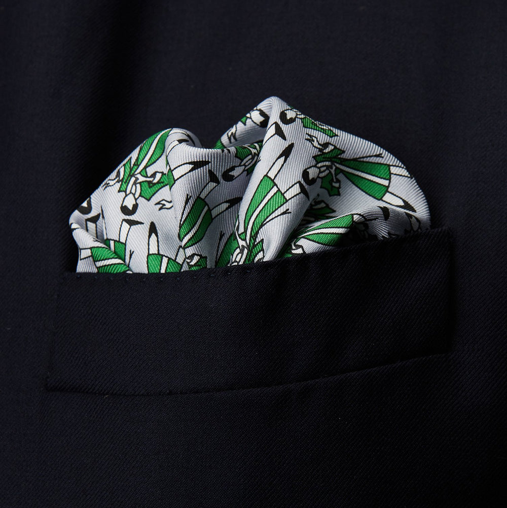 The Turnbull & Asser Green Dressing Gowns Pocket Square features a white silk base with green lines and a repeating pattern of green and black illustrated golfers, inspired by classic Turnbull dressing gown designs.