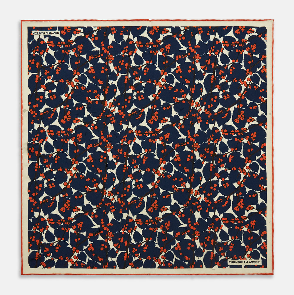 The Blue Berry Floral Pocket Square by Turnbull & Asser features a navy blue silk background with red berry and white leaf designs, plus small labels on two corners—making it a perfect festive gift.