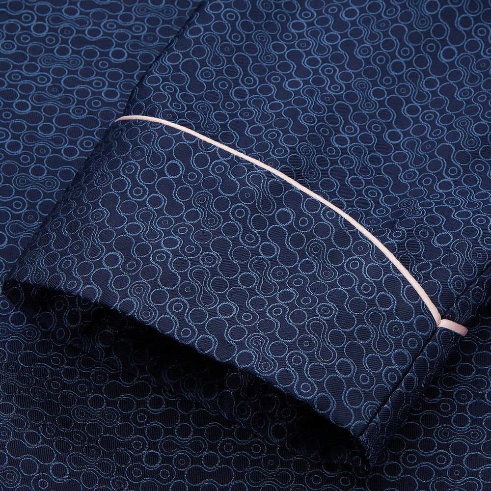 The Turnbull & Asser Blue Multi Circle Silk Jacquard Gown features a subtle geometric pattern, white piping, a chest pocket, and a matching waist belt, all showcased against a white background.