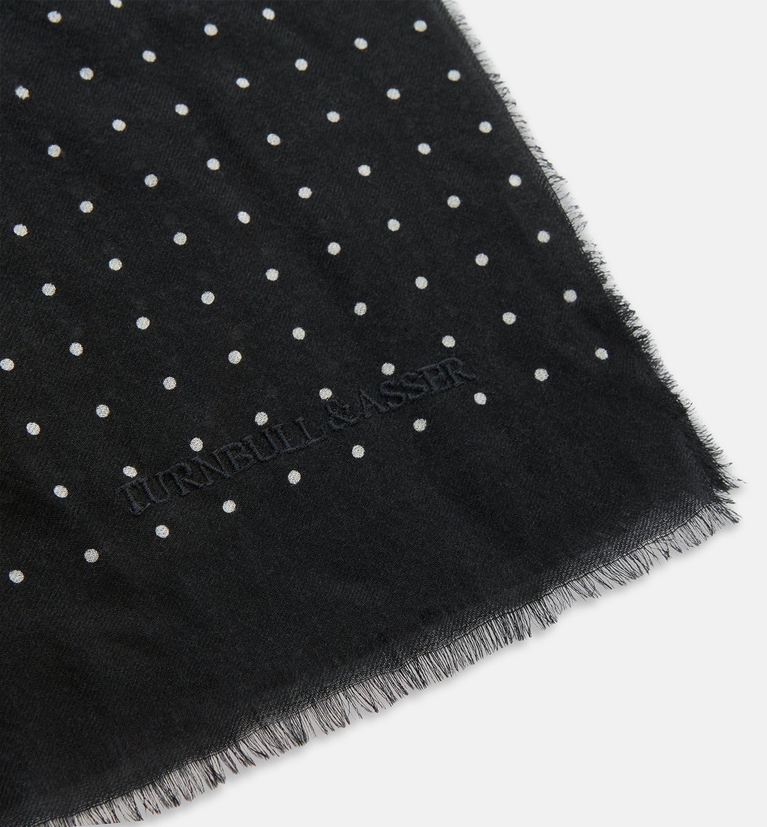 View 2 of product The Turnbull & Asser Black & White Spot Superfine Cashmere Scarf features evenly spaced white dots, lightly frayed edges, and a lightweight design for subtle elegance in any outfit. Shown laid flat with a loose knot at the top.