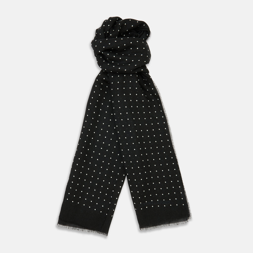 The Turnbull & Asser Black & White Spot Superfine Cashmere Scarf features evenly spaced white dots, lightly frayed edges, and a lightweight design for subtle elegance in any outfit. Shown laid flat with a loose knot at the top.