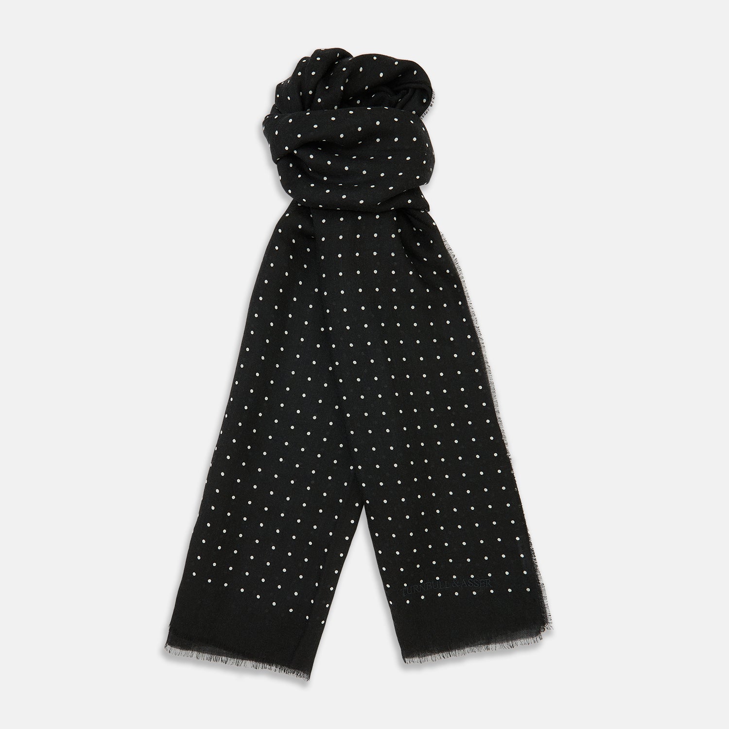 View 1 of product The Turnbull & Asser Black & White Spot Superfine Cashmere Scarf features evenly spaced white dots, lightly frayed edges, and a lightweight design for subtle elegance in any outfit. Shown laid flat with a loose knot at the top.