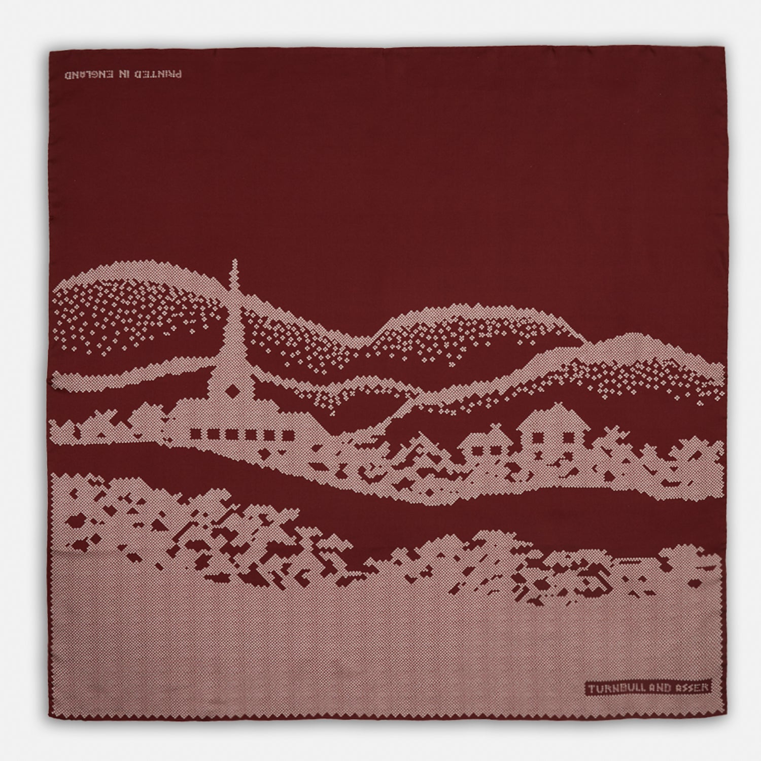 View 1 of product The Burgundy Snowscape Motif Silk Extra Large Scarf by Turnbull & Asser features a hand-rolled edge and a pink cross-stitch village scene—houses, church, hills—printed in England. A refined winter accessory.