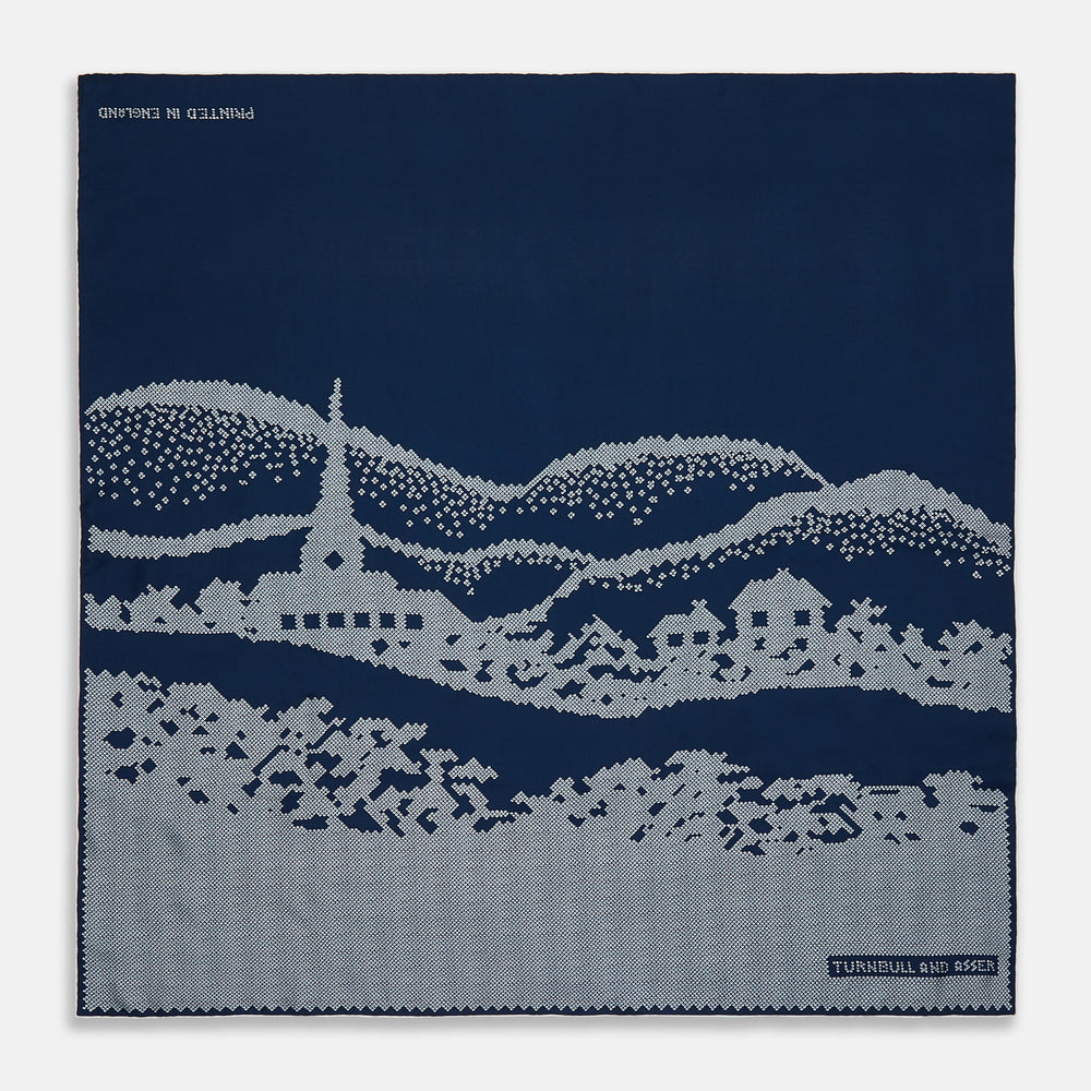 The Blue Snowscape Motif Silk Extra Large Scarf by Turnbull & Asser features a light blue village scene and hand-rolled edges, with TURNBULL AND ASSER at the bottom right and PRINTED IN ENGLAND at the top left.