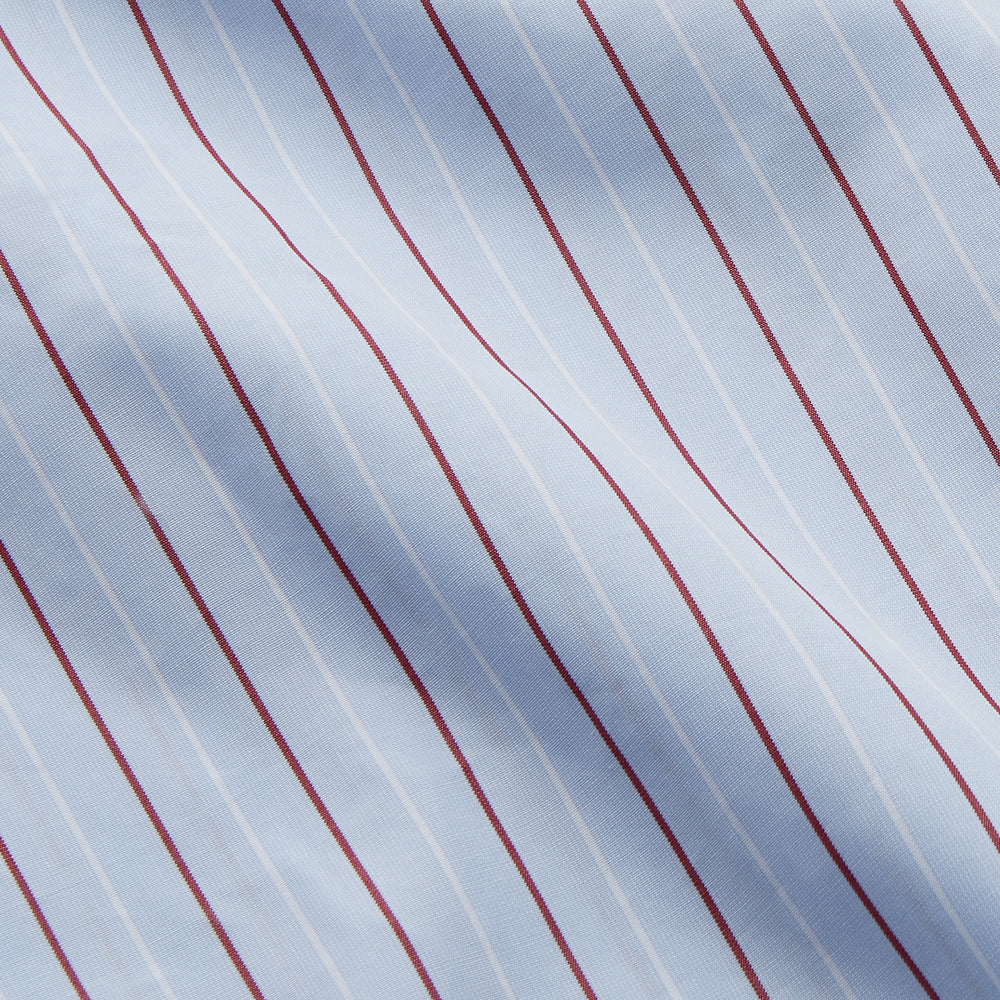 The Turnbull & Asser Burgundy Stripe Regular Fit Shirt features a T&A collar, double cuffs, and white buttons. Made from light blue Italian cotton poplin with vertical burgundy and white pinstripes. Laid flat on a white background.