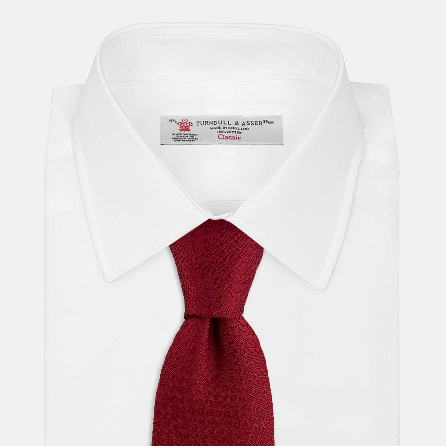 View 2 of product The Turnbull & Asser Burgundy Abstract Tonal Silk Jacquard Tie is shown rolled up with a subtle textured pattern on a plain white background—an elegant formalwear choice.