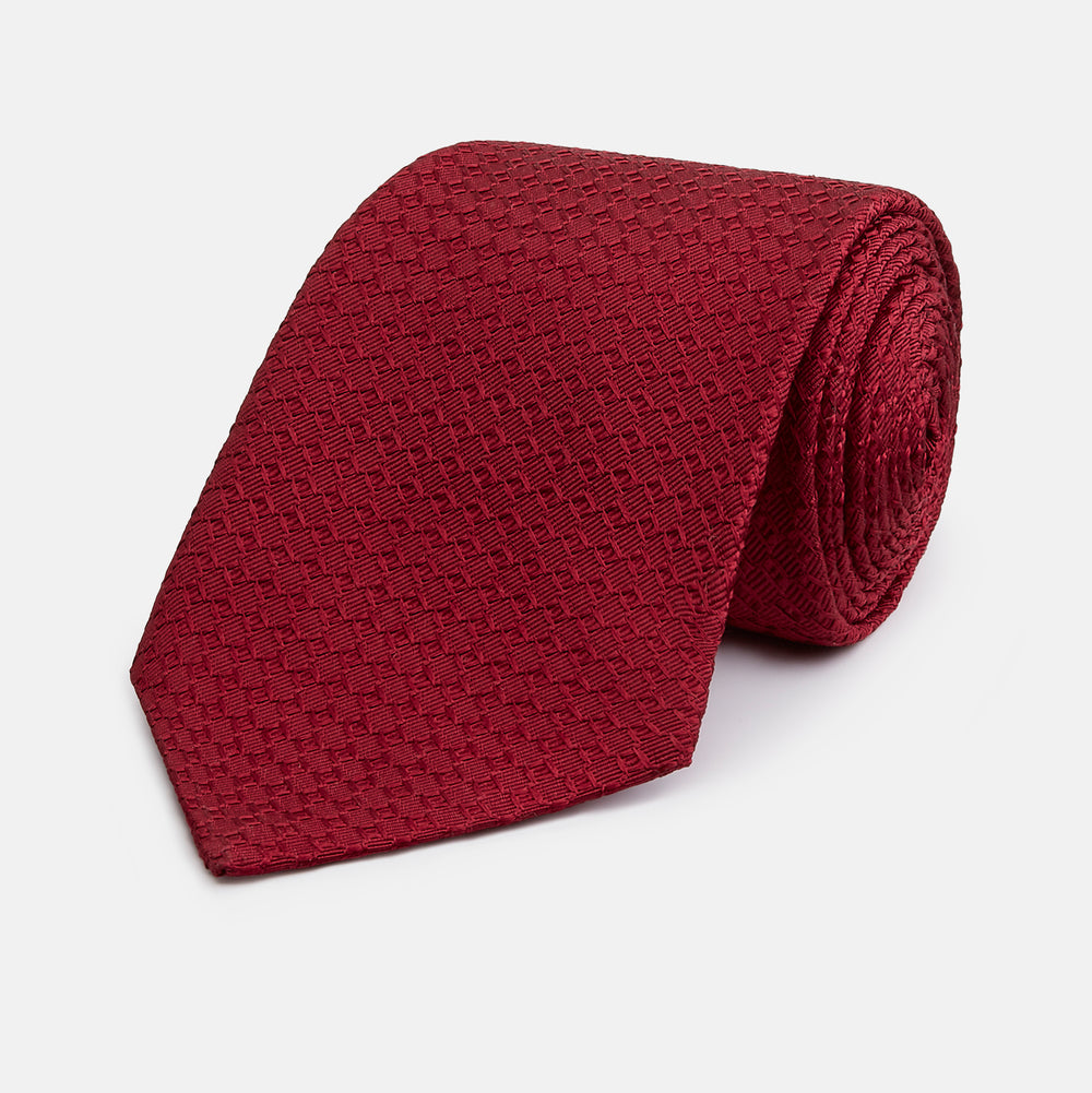 The Turnbull & Asser Burgundy Abstract Tonal Silk Jacquard Tie is shown rolled up with a subtle textured pattern on a plain white background—an elegant formalwear choice.