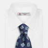 View 2 of product The Turnbull & Asser Blue Geometric Jacquard Tie is a rolled-up silk tie showcasing a repeating light blue and white geometric floral pattern with dotted accents, set against a plain light background.