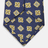 View 4 of product The Turnbull & Asser Yellow Geometric Jacquard Tie in navy features a repeating pattern of yellow geometric shapes with blue accents, presented rolled up on a white background.