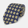 View 1 of product The Turnbull & Asser Yellow Geometric Jacquard Tie in navy features a repeating pattern of yellow geometric shapes with blue accents, presented rolled up on a white background.