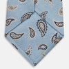 View 4 of product The Turnbull & Asser Sky Blue Renoir Paisley Tie, crafted in silk with a repeating navy and beige pattern, is shown rolled up with its pointed end forward on a plain white background.