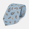 View 1 of product The Turnbull & Asser Sky Blue Renoir Paisley Tie, crafted in silk with a repeating navy and beige pattern, is shown rolled up with its pointed end forward on a plain white background.
