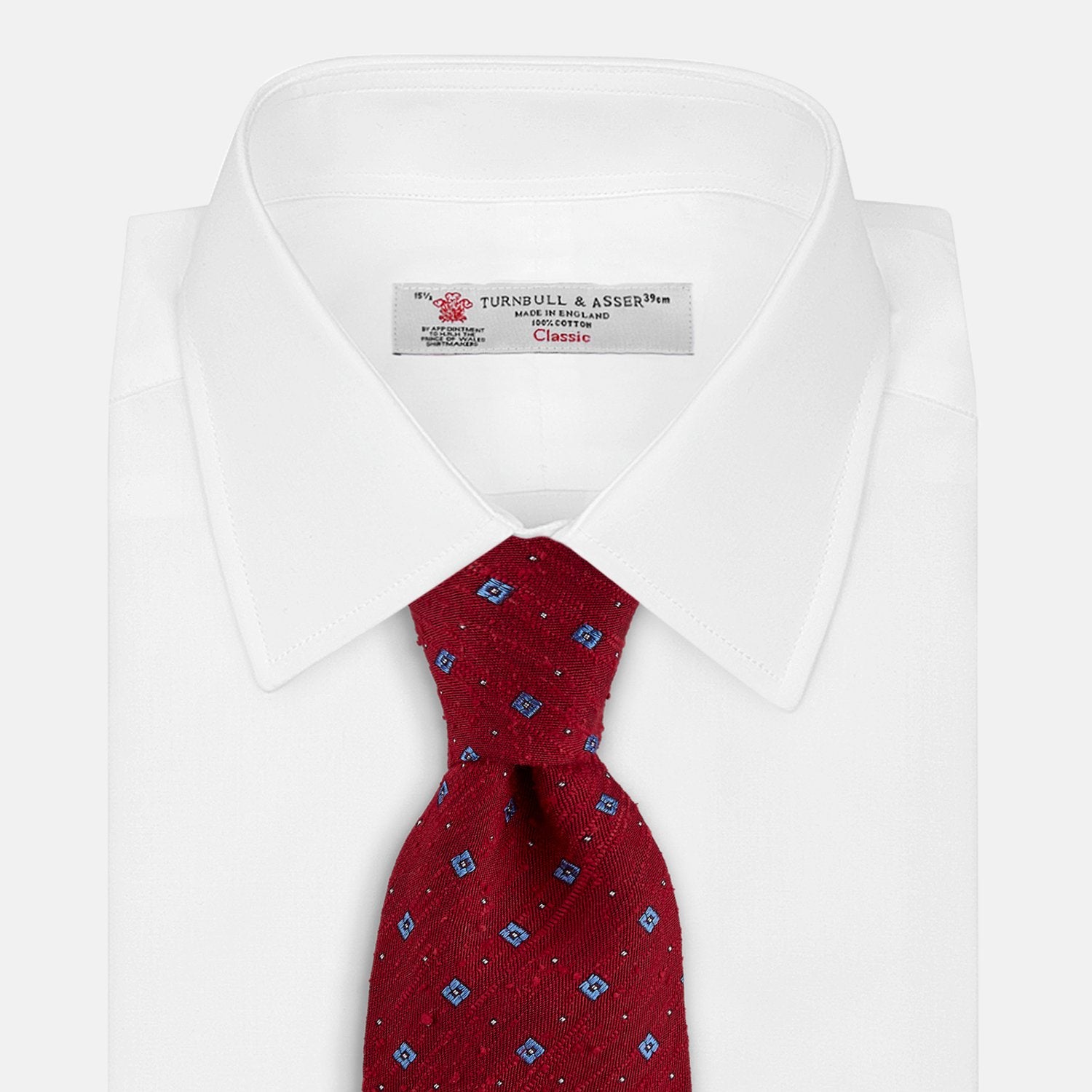View 2 of product The Turnbull & Asser Red Square Silk Tie features a red and blue pattern with small white squares, elegantly rolled and displayed on a plain white background—a refined choice for men's accessories.