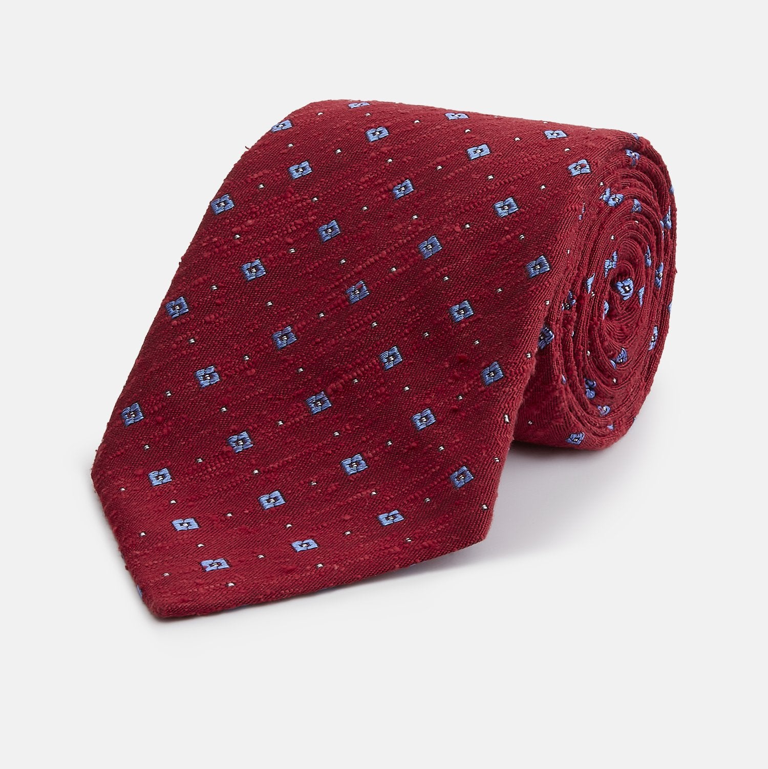 View 1 of product The Turnbull & Asser Red Square Silk Tie features a red and blue pattern with small white squares, elegantly rolled and displayed on a plain white background—a refined choice for men's accessories.
