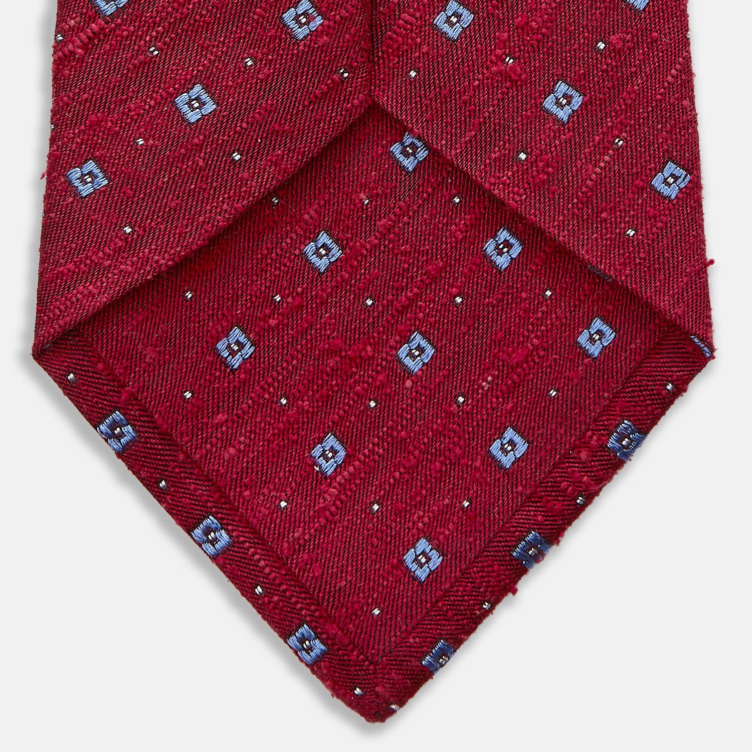View 4 of product The Turnbull & Asser Red Square Silk Tie features a red and blue pattern with small white squares, elegantly rolled and displayed on a plain white background—a refined choice for men's accessories.