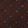 View 3 of product The Turnbull & Asser Brown Square Silk Tie, featuring a jacquard pattern of small blue squares and dots, is shown rolled up on a plain white background.