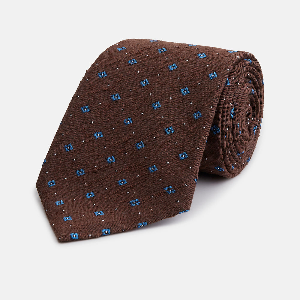 The Turnbull & Asser Brown Square Silk Tie, featuring a jacquard pattern of small blue squares and dots, is shown rolled up on a plain white background.