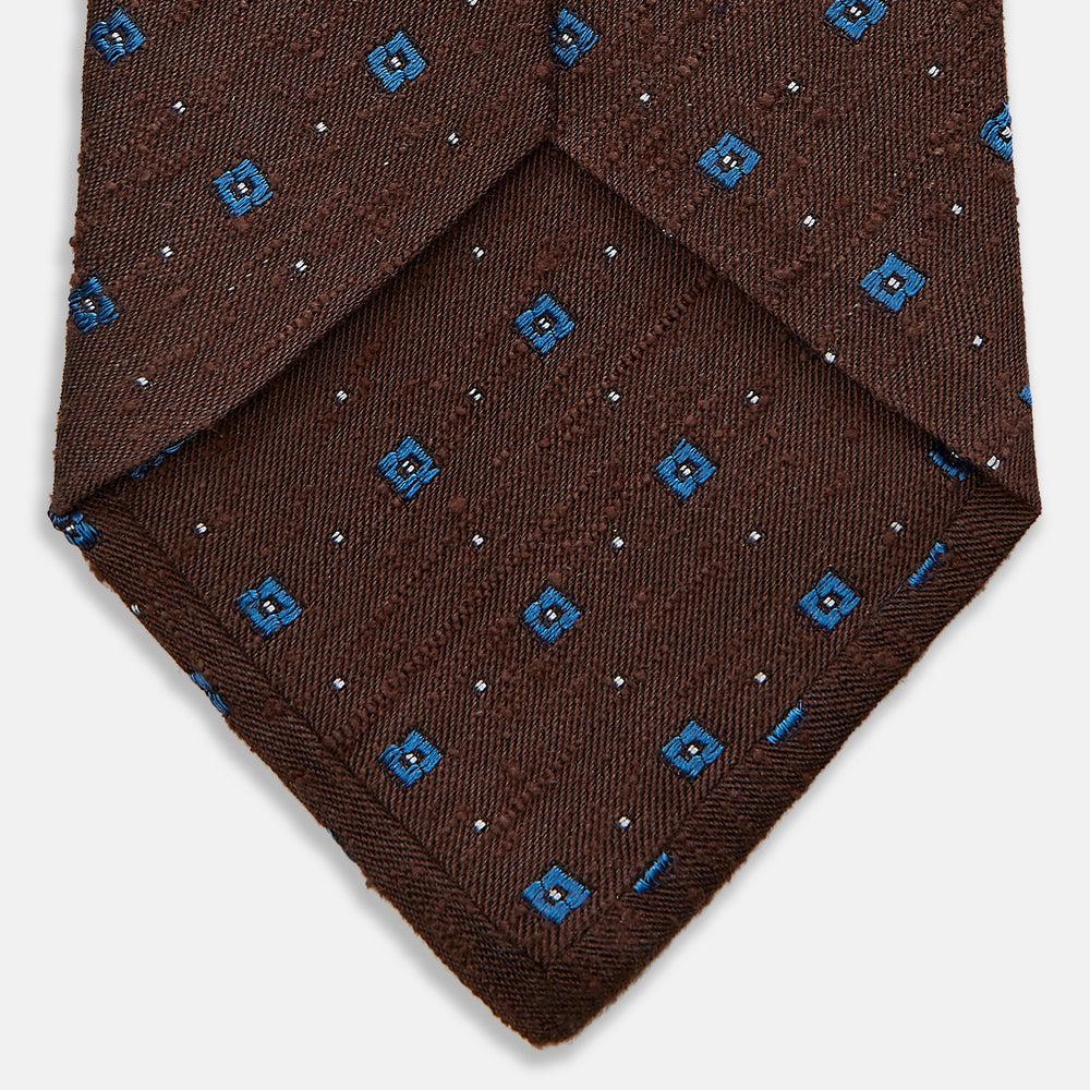 The Turnbull & Asser Brown Square Silk Tie, featuring a jacquard pattern of small blue squares and dots, is shown rolled up on a plain white background.
